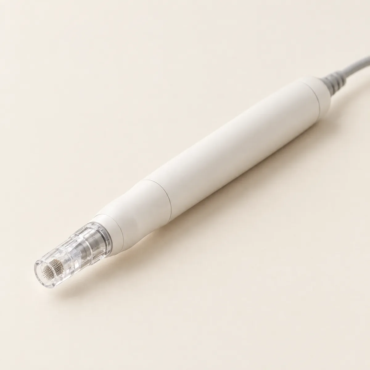 A slim white microneedling pen with a clear needle cartridge, on a cream background